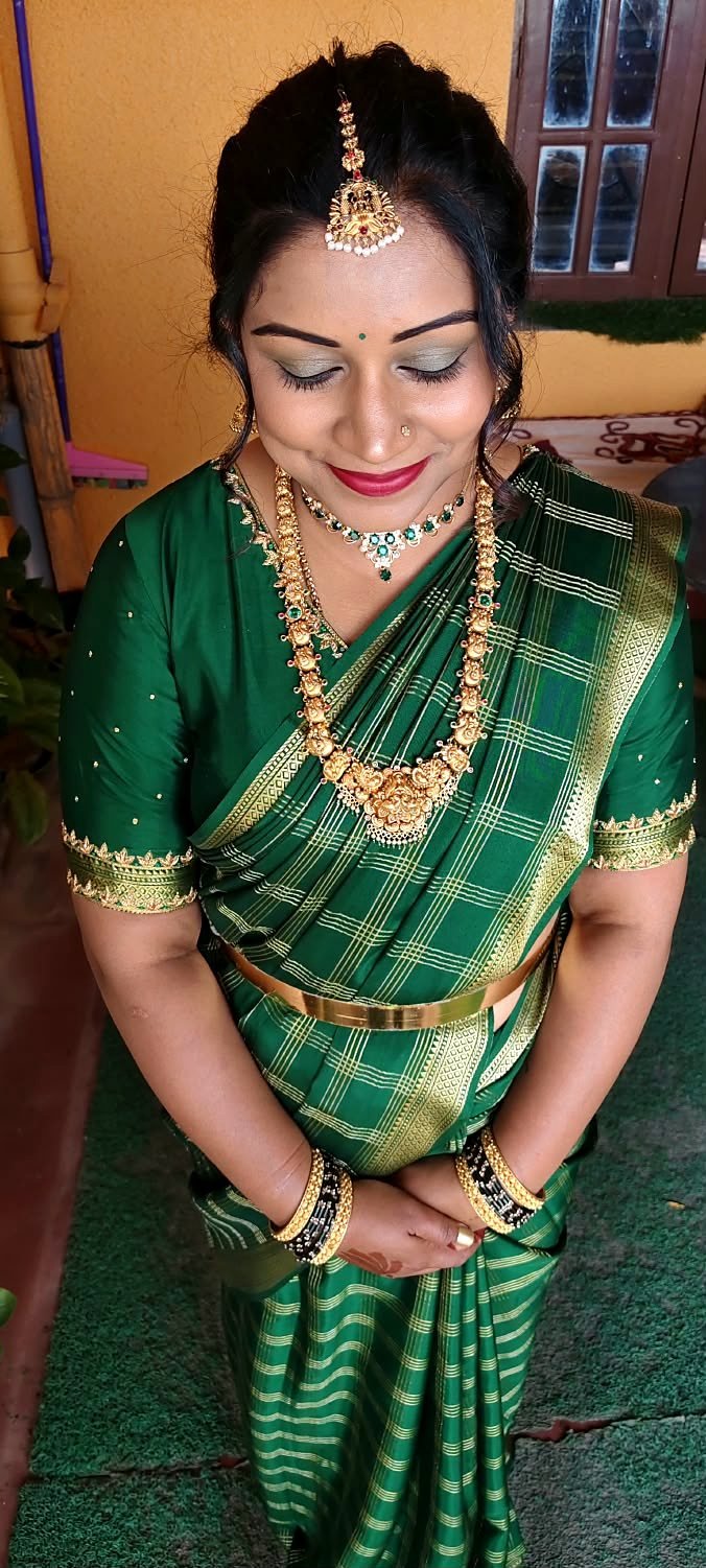 Woman in a green silk saree looking down, showing soft green shimmer eye makeup, defined brows and red lips